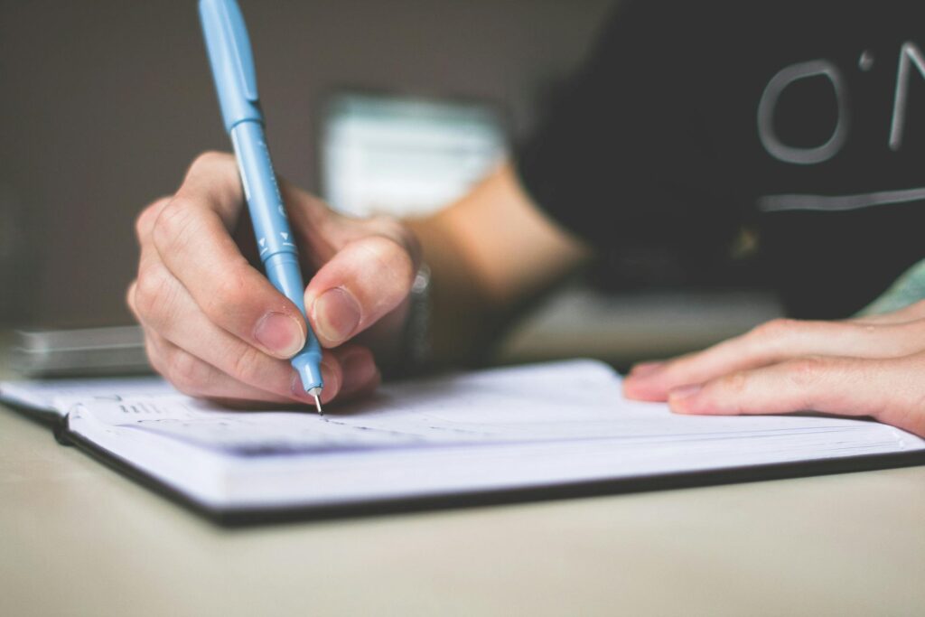 يد تكتب في دفتر بقلم أزرق، تعبّر عن التأمل والكتابة الشخصية في رسالة الموقع